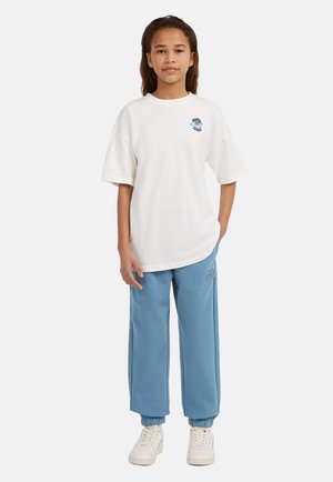 Vit oversized t-shirt med en blå grafik, kombinerad med ljusblå sweatshirtbyxor med en broderad detalj. Vita sneakers fulländar outfiten.