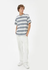 Randig t-shirt i ljusgrått med marinblå ränder, rund halsringning, korta ärmar; kombinerad med vita byxor och vita sneakers.