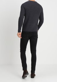 Sweter z prążkowanego węgla o okrągłym dekolcie i długich rękawach, w połączeniu z slim fit czarnymi dżinsami i ciemnobrązowymi botkami za kostkę.