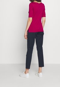 Fuksia, lyhythihainen paita, jossa on pyöreä kaula-aukko, yhdistettynä tummansinisiin, slim fit -housuihin ja valkoisiin lenkkareihin. Sileä kangas, ilman näkyviä kuvioita.