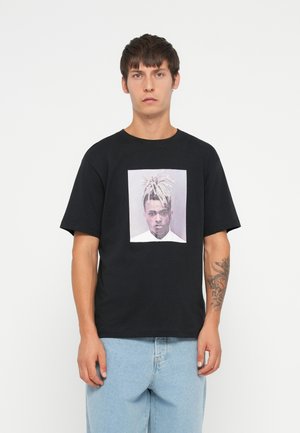 Black cotton t-shirt featuring a graphic print of a person on the front. The shirt has a relaxed fit and short sleeves.
