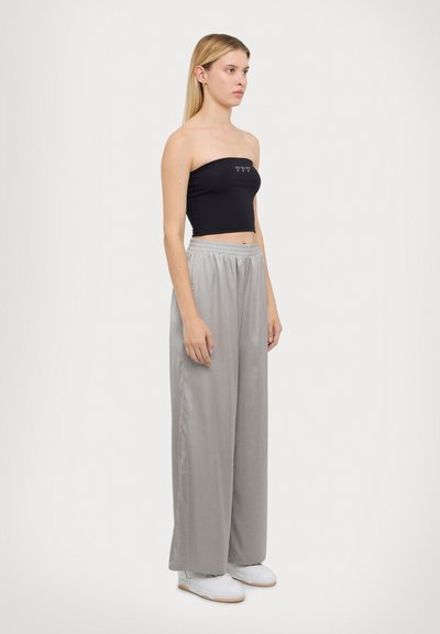 Haut sans manches noir avec des coutures beige, associé à un pantalon large gris clair. La tenue présente une texture lisse et un léger éclat.