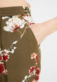 Shorts à imprimé floral en vert olive, dotés d'un tissu léger, d'une ceinture élastique et de poches latérales avec des fleurs rouges et blanches éclatantes.