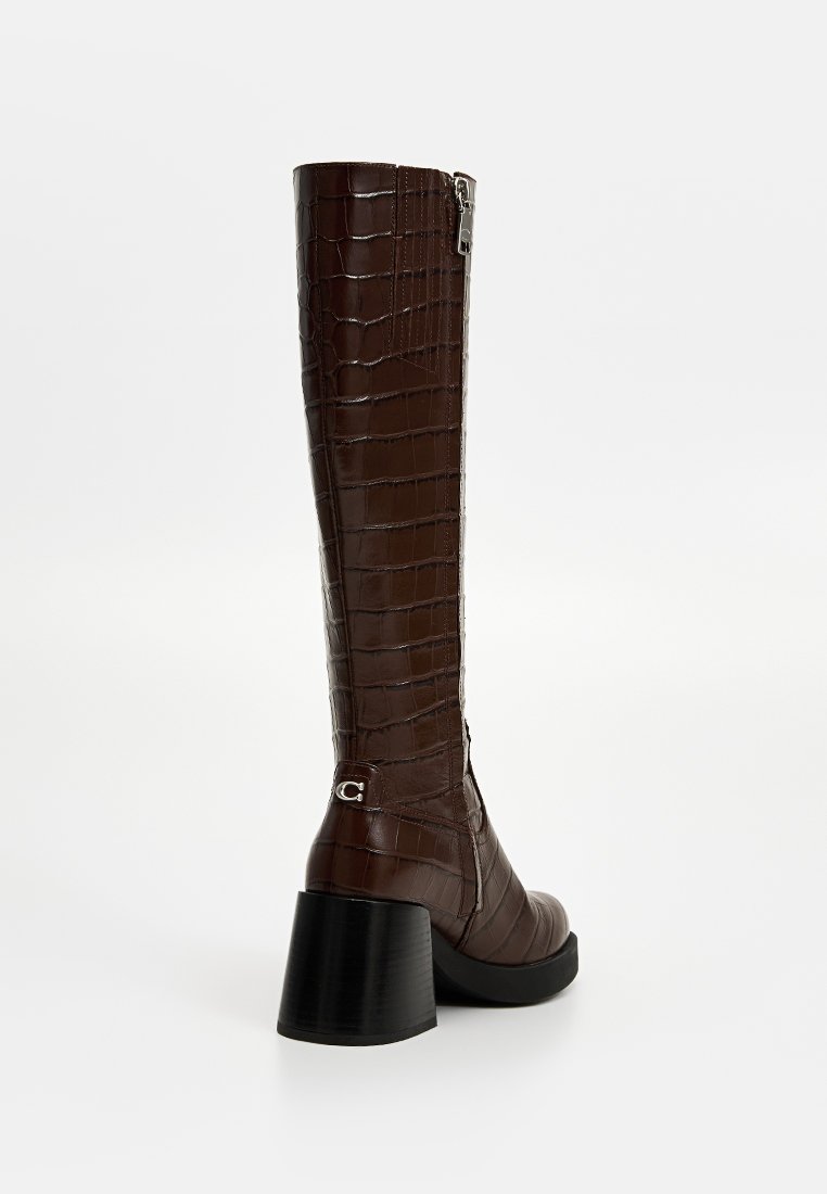 Stivale alto in finta pelle marrone con texture cocco, dettaglio argentato alla caviglia e tacco spesso nero. Chiusura laterale per un facile indossamento.