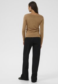 Maglione marrone a maniche lunghe con scollatura ampia, realizzato in un materiale morbido. Pantaloni neri a vita alta con taglio dritto, tasche visibili.