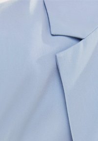 Ljust blått tyg med en slät textur, med skarpa, vinklade kragekanter och subtila diagonala sömnadsmönster.