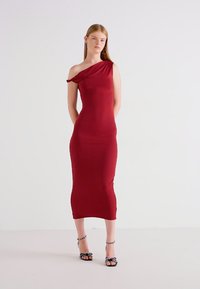Burgundimidi mekko, jossa on yksi olkaimen muotoilu, kapea istuvuus ja sujuva pinta. Mallilla on päällään musta-valkoiset raidalliset korkokengät.