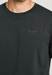 T-shirt in cotone nero con scollatura rotonda e maniche corte. Presenta un piccolo logo grigio chiaro sul lato sinistro del petto.