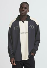 Langærmet skjorte med et sort og creme stribet design, der har numrene "19" og "93" samt teksten "KEEP MOVING FORWARD" i grå. Kraven er kontrastfarvet.