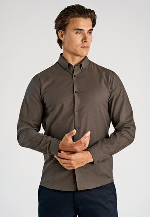 Bruine blouse met knopen, een brede kraag, lange mouwen en een gladde textuur; heeft zwarte knopen en een aansluitend ontwerp.