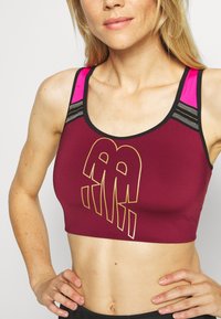 Sostenitore sportivo bordeaux con logo dorato, dotato di spalline rosa e dettagli neri. Realizzato in tessuto morbido, progettato con una vestibilità corta.