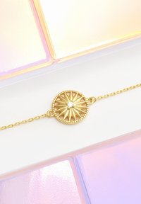 Guldarmband med ett cirkulärt hänge med solstråle-design och en central ädelsten. Kedjelänkarna är känsliga och jämnt storlek.