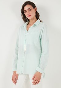 Light mint green button-up shirt in a breathable fabric, featuring a chest pocket and long sleeves, with a subtle textured pattern.