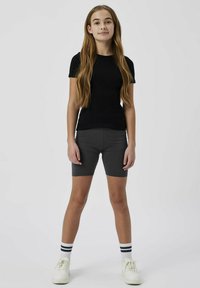 T-shirt ajustée noire à manches courtes associée à un short de cyclisme gris et à des baskets blanches avec des chaussettes rayées noires. Tissu lisse, design simple.