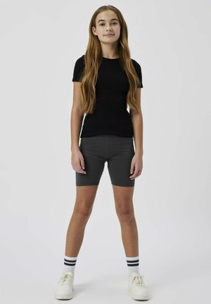Czarna, dopasowana koszulka z krótkim rękawem w połączeniu z szarymi szortami rowerowymi i białymi sneakersami z czarnymi skarpetkami w paski. Gładki materiał, prosty design.