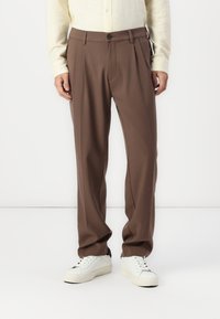 Brown pleated trousers with a straight fit, made from smooth fabric, featuring a button closure and side pockets. Styled with white sneakers.