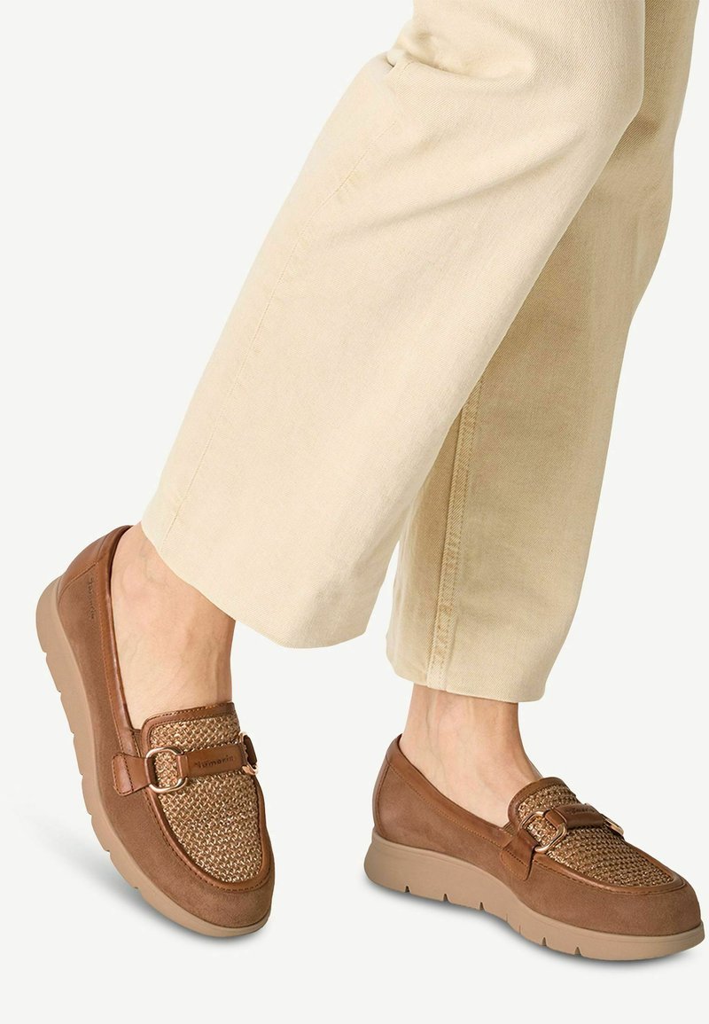 Scarpe slip-on marroni con parte superiore intrecciata, caratterizzate da un tessuto testurizzato e da una fibbia decorativa. La suola è di colore chiaro e spessa.