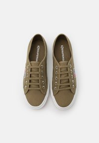 Sneaker in tela verde oliva con suole in gomma bianca, punta rotonda e sei paia di occhielli in argento; presenta il marchio "Superga" all'interno e sul lato.