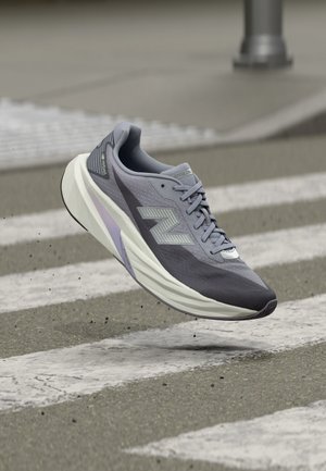 Grauer und weißer New Balance Laufschuh schwebt über einem gepflasterten Zebrastreifen mit weißen Streifen.