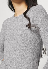 Maglione grigio a maglia con scollo rotondo, maniche lunghe e una texture morbida. Presenta una vestibilità rilassata e un design minimalista.