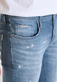 Vaqueros de denim azul claro con un acabado desgastado, bolsillos frontales y una etiqueta metálica en el bolsillo trasero.