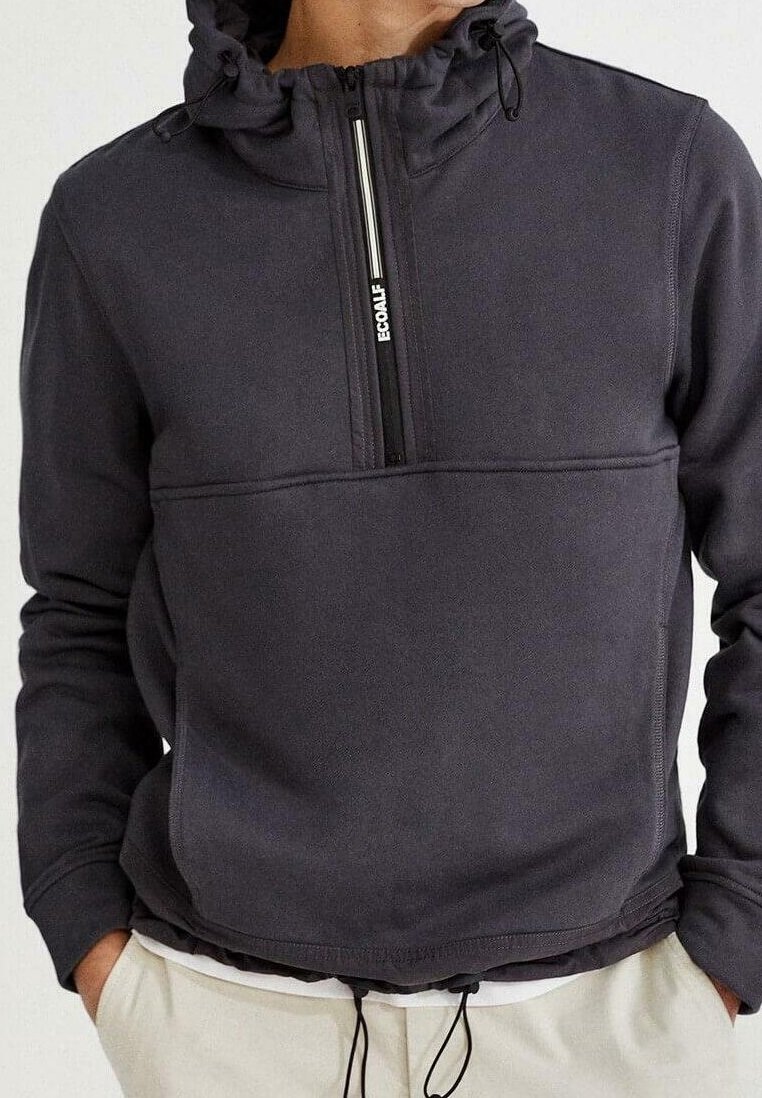 Sudadera negra con capucha tipo pulóver, media cremallera frontal, capucha con cordón y cinturilla. Textura suave y diseño minimalista con un bolsillo delantero.