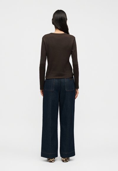 Καφέ πουκάμισο με μακριά μανίκια σε συνδυασμό με μαύρο τζιν παντελόνι ψηλόμεσο, φαρδύ στο πόδι. Διακριτικές ραφές και παπούτσια με animal print.