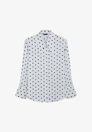 Weißes Hemd mit schwarzen Punkten, ausgestattet mit einem spitzen Kragen und langen Ärmeln mit geknöpften Manschetten. Glatte Stoffoberfläche.