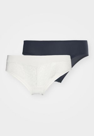 Dva páry dámskeho spodného prádla: jedny biele s krajkovými detailmi a jedny jednofarebné námornícke modré. Obe majú bezšvový dizajn a jemnú tkaninu.