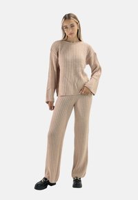 Conjunto de ropa de descanso de punto acanalado beige, que incluye una camiseta de manga larga con cuello ancho y pantalones a juego. Textura suave con un ajuste relajado. Zapatos de plataforma negros.