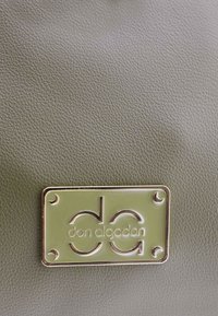 Cuero verde oliva texturizado con una placa rectangular de metal en tono dorado que presenta el logo "don algodón" y detalles decorativos en las esquinas.