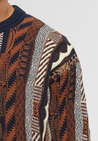 Maglione a maglia con motivi intricati in marrone, blu navy e crema, con sezioni strutturate e varianti nei punti.