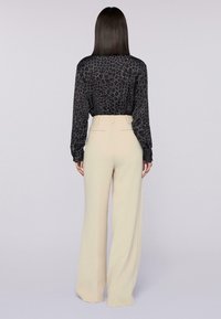 Zwarte blouse met lange mouwen en een geometrisch patroon, gecombineerd met hoog uitgesneden, brede beige broek. Glad oppervlak en een op maat gemaakte pasvorm.