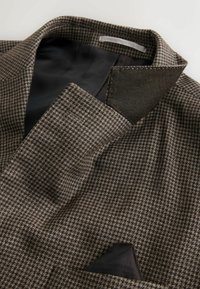 Textured brown tweed fabric with a houndstooth pattern and a contrasting black collar. Includes a small inner pocket.