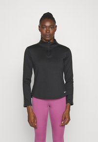 Zwarte rits-up langmouwtop met een hoge kraag en zijpatronen, gecombineerd met roze leggings. Zachte stof met een aansluitend ontwerp.