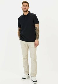 Mørkeblå polo skjorte med tekstureret design, korte ærmer og krave, parret med beige bukser og hvide sneakers.