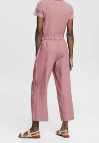 Roze linnen jumpsuit met korte mouwen, elastische tailleband en een brede broekspijpdesign. Draag het met lichtbruine sandalen met een platte zool.