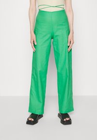 Zielone szerokie spodnie w gładkim, lekkim materiale z wysokim stanem; dobrane z czarnymi sandałami na grubej podeszwie.