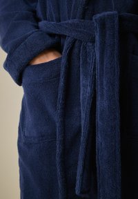 Granatowy szlafrok kąpielowy z frotte, z wi�ązanym paskiem, o teksturowanym wykończeniu i dwóch bocznych kieszeniach. Materiał wydaje się być miękki i chłonny.