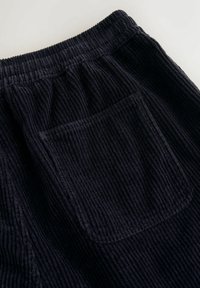 Marineblauwe corduroy broek met een geribbelde textuur, elastische tailleband en een enkele achterzak. Zachte stof met duidelijke stikdetails.