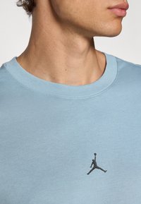 Lys blå bomulls t-skjorte med ribbet rund hals og en svart Jordan-logo trykt på brystet. Glatt tekstur og uformell design.