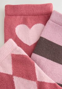 Tre paia di calze: uno con un motivo a cuori rosa, uno con strisce rosa e marrone chiaro, e uno con un motivo a diamanti rosa.