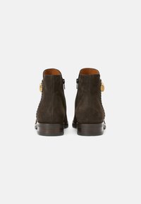 Paire de bottines en daim marron foncé avec talons bas empilés, fermeture éclair arrière et tirettes de fermeture éclair dorées sur un fond blanc uni.