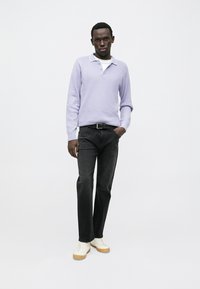 Polo suéter color lila claro, jeans negros y zapatillas blancas con suelas de goma. Diseño sencillo, tejido texturizado y ajuste clásico.