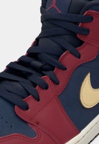 Gros plan d'une basket rouge et bleu marine avec des lacets bleu marine, un swoosh Nike beige et un logo Jumpman rouge sur la languette.