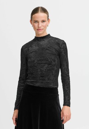 Maglietta nera a maniche lunghe con un motivo floreale testurizzato, collo alto e design aderente, abbinata a una gonna di velluto nera.