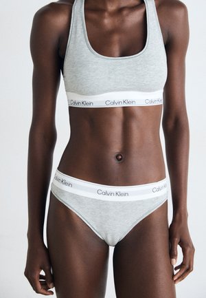 Grijze katoenen sportbeha en bikini-set, met een witte elastische band met "Calvin Klein"-branding. Glad textuur en aansluitend ontwerp.