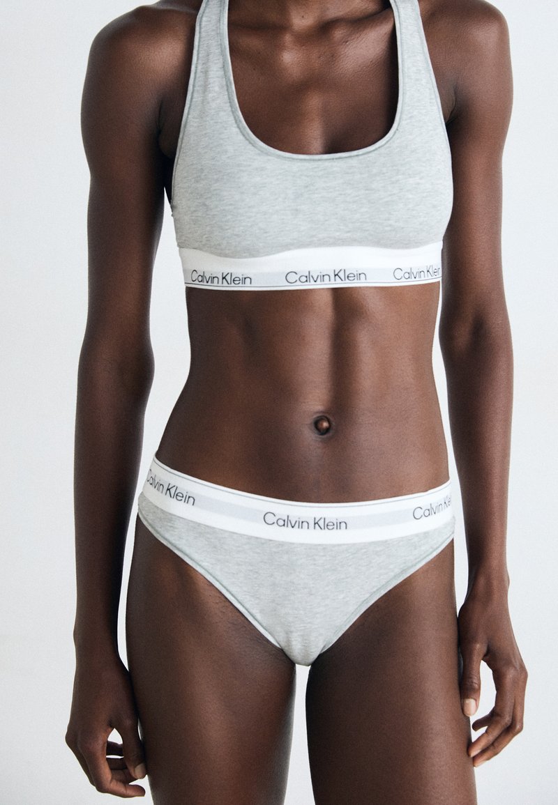 Grijze katoenen sportbeha en bikini-set, met een witte elastische band met "Calvin Klein"-branding. Glad textuur en aansluitend ontwerp.