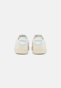 Witte leren sneakers met lichtbeige accenten, voorzien van een textuur rubberen zool en "Reebok" branding in het blauw op de hiel en de tong.