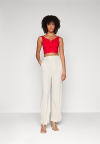 Top corto rosso con scollo a V e dettagli arricciati, abbinato a pantaloni ampi color crema e tacchi a strappo trasparenti.